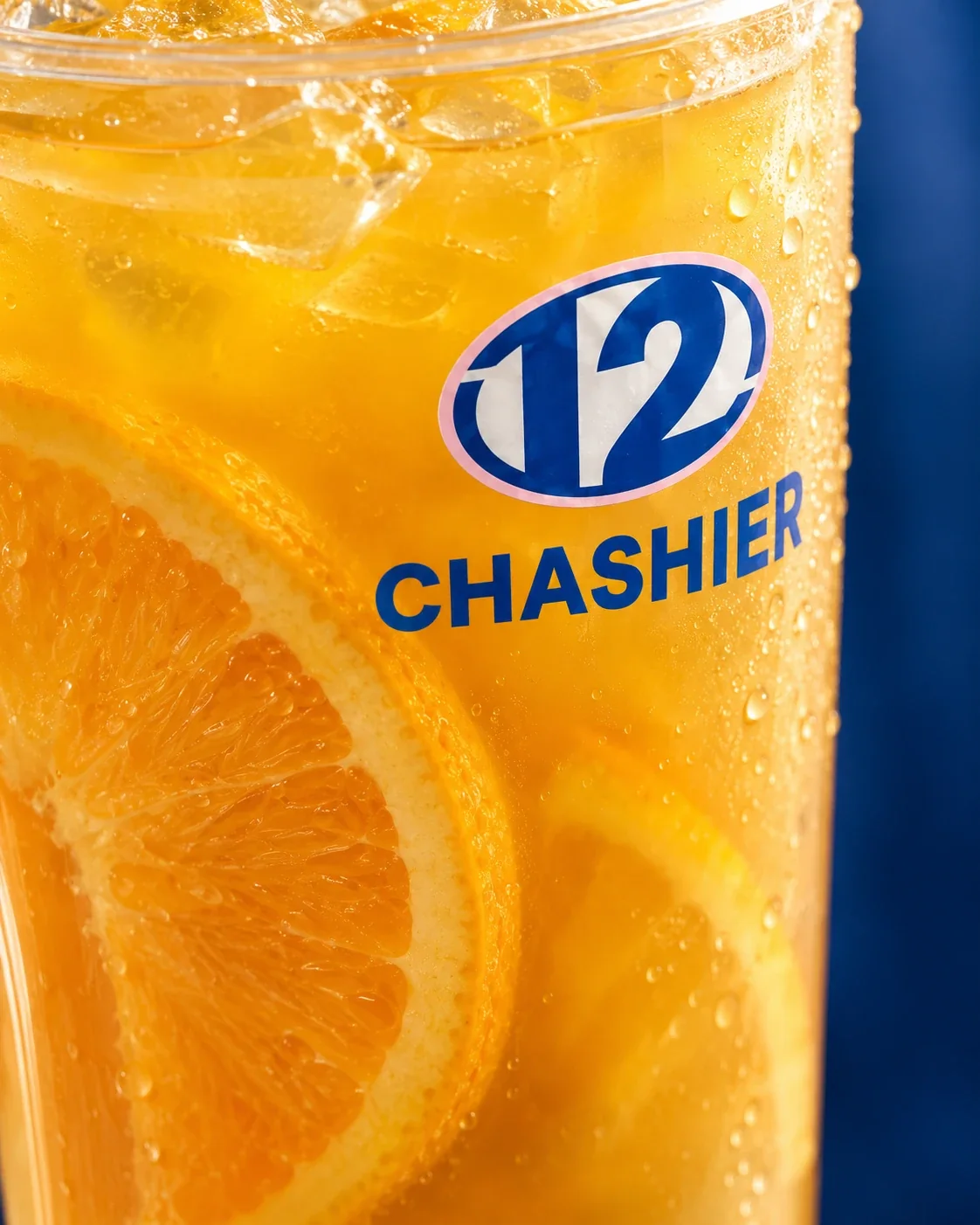 Té de naranja de Chashier con rodajas de naranja y hielo, con el logo del 12 en el vaso, sobre fondo azul.